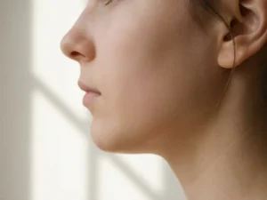 Profiel van een jonge persoon met gladde huid en zachte natuurlijke belichting tegen een minimalistische witte achtergrond