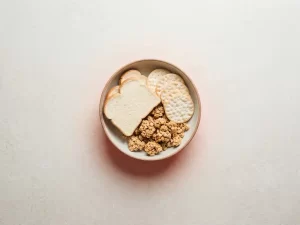 Kom met witbrood, crackers en suikerhoudende granola op stenen ondergrond, met roodachtig gloed die ontstekingsreactie symboliseert.