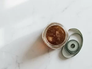 Glazen pot donkergele kristalliserende honing op wit marmer met een opgerolde meetlint, bovenaanzicht.