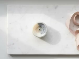 Uitgebrande kaars op wit marmer, de vlam gedoofd, gefotografeerd van bovenaf in zacht natuurlijk licht met een lange subtiele schaduw.